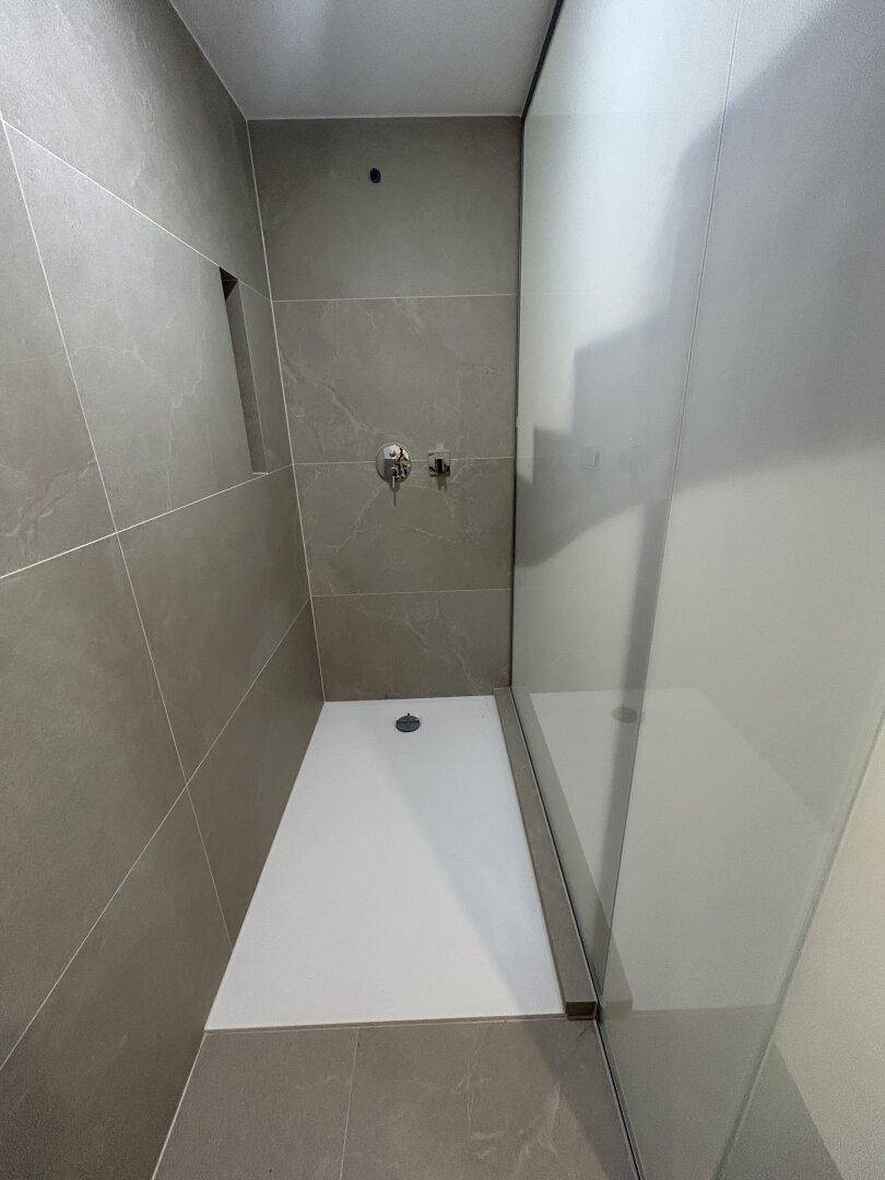 Moderne begehbare Dusche mit großformatigen grauen Fliesen und minimalistischem Design.
