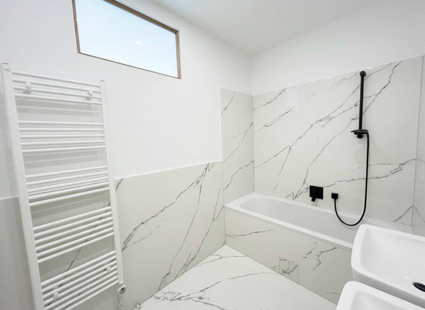 Modernes Badezimmer mit Marmoroptik-Fliesen, Badewanne und beheiztem Handtuchhalter.