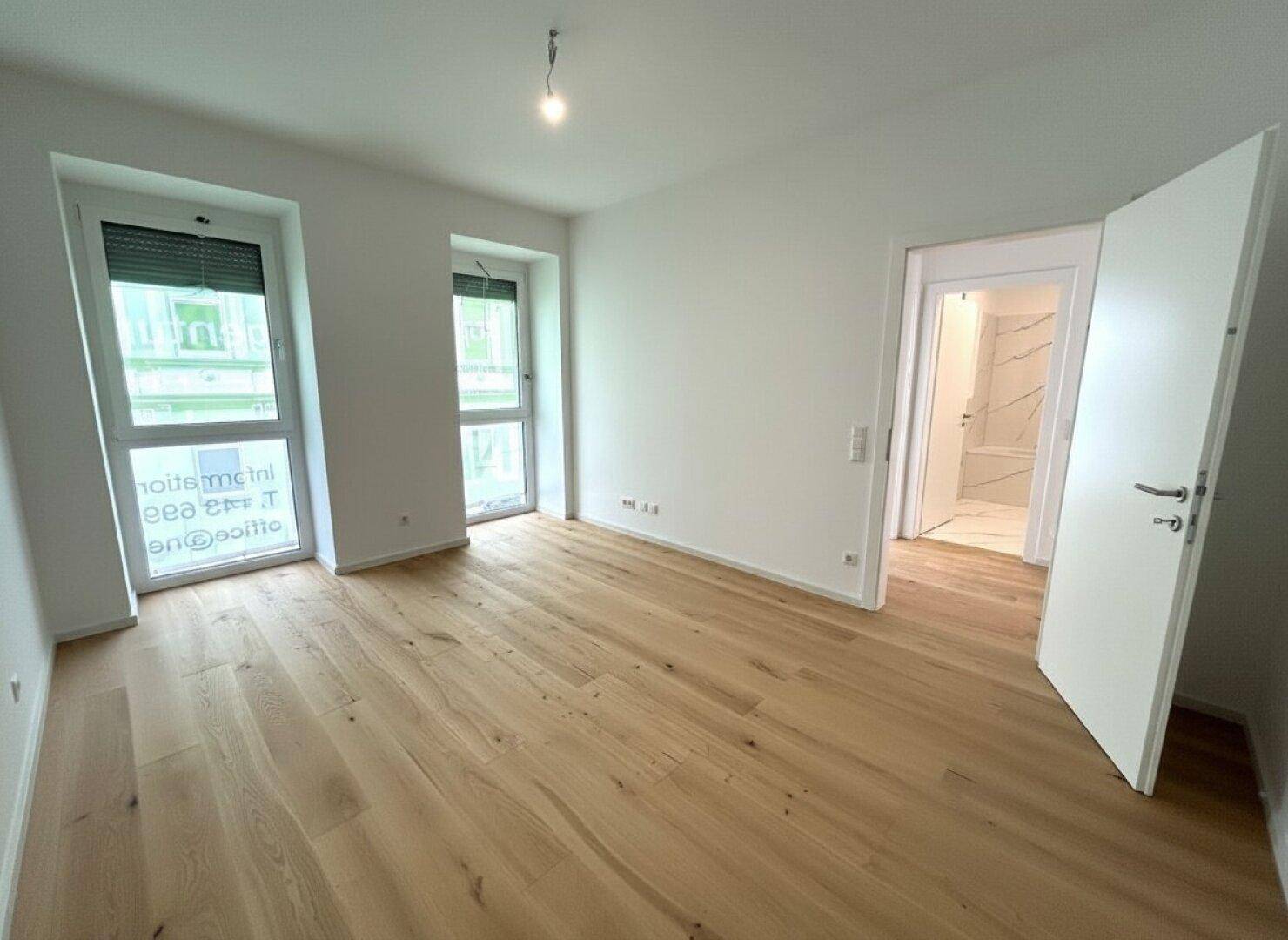 Schlafzimmer mit Holzboden und Fenstern, die den Raum mit natürlichem Licht versorgen, mit Badzugang.