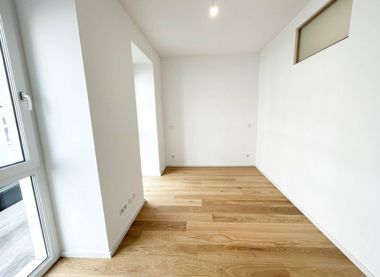 Leeres Zimmer mit Holzboden und hohen Fenstern, die viel Tageslicht in den Raum lassen.