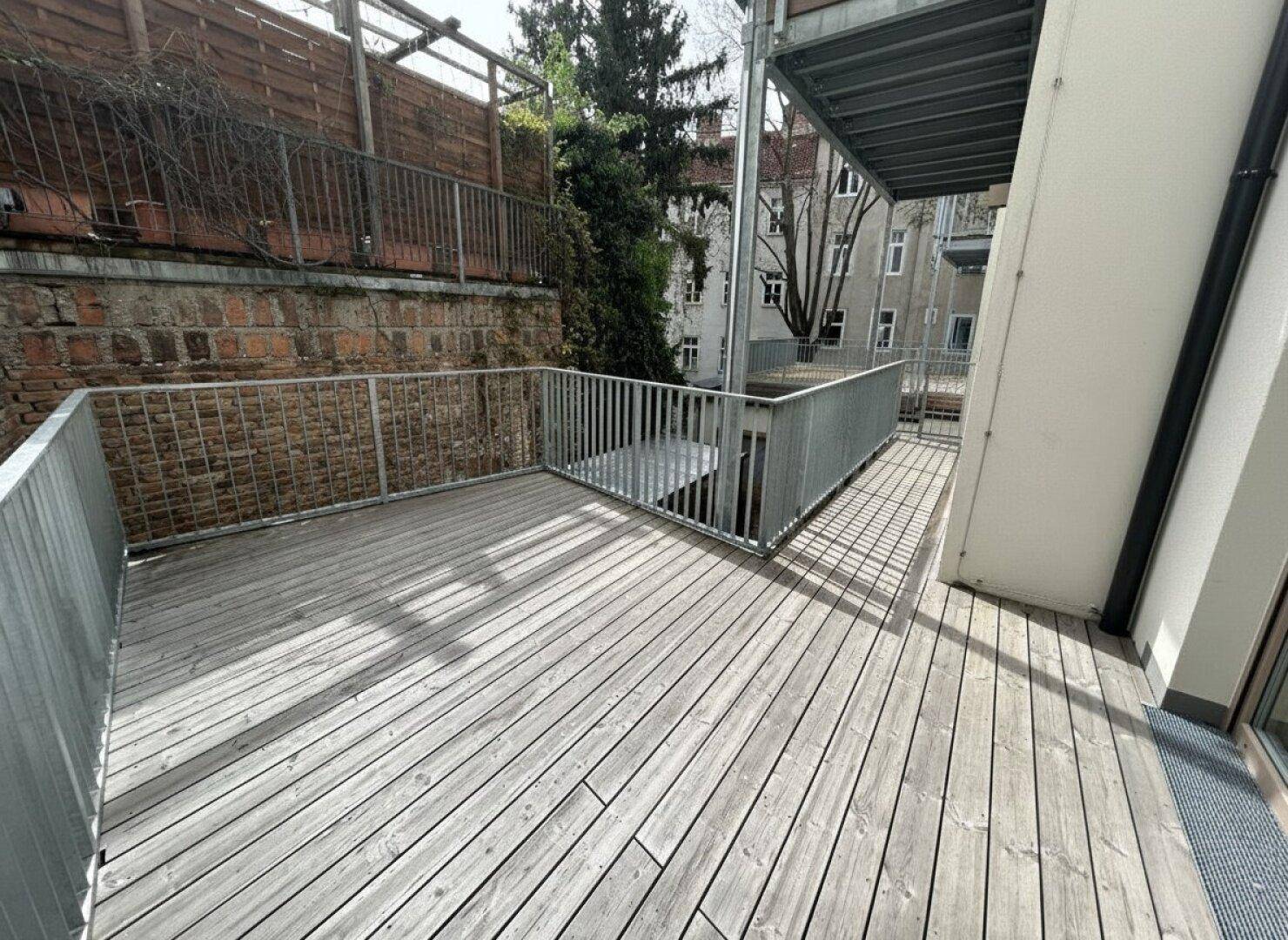 Geräumige Holzterrasse mit Metallgeländer, umgeben von einer Ziegelmauer und Grün.