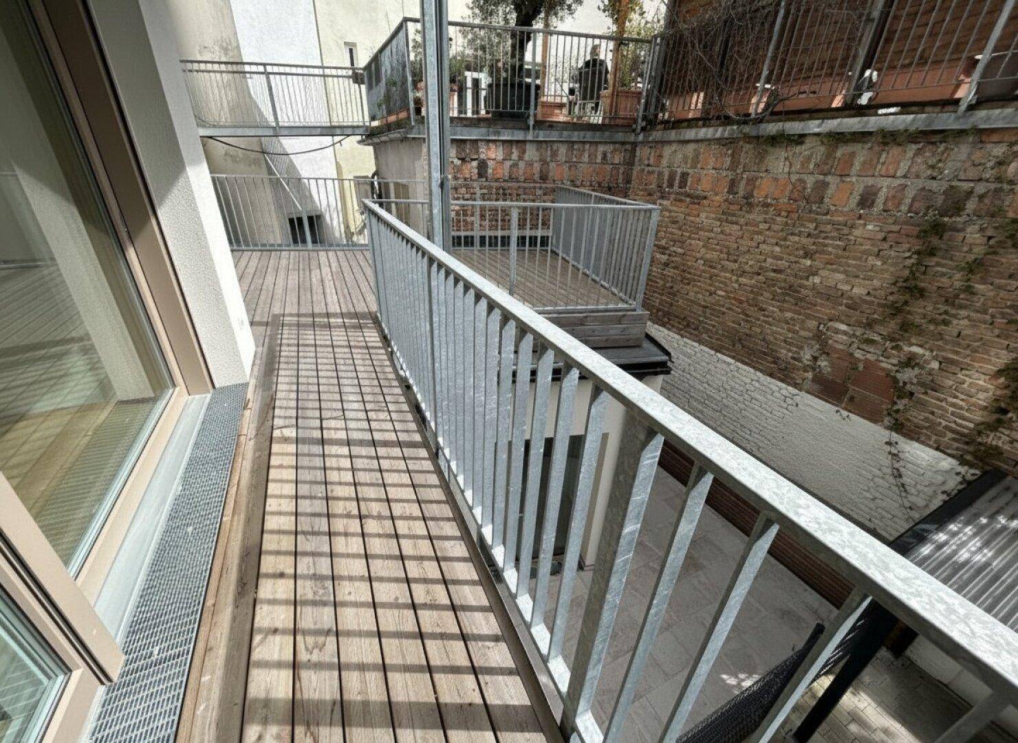Schmaler Balkon mit Holzboden und Metallgeländer, bietet einen Blick auf die Umgebung.