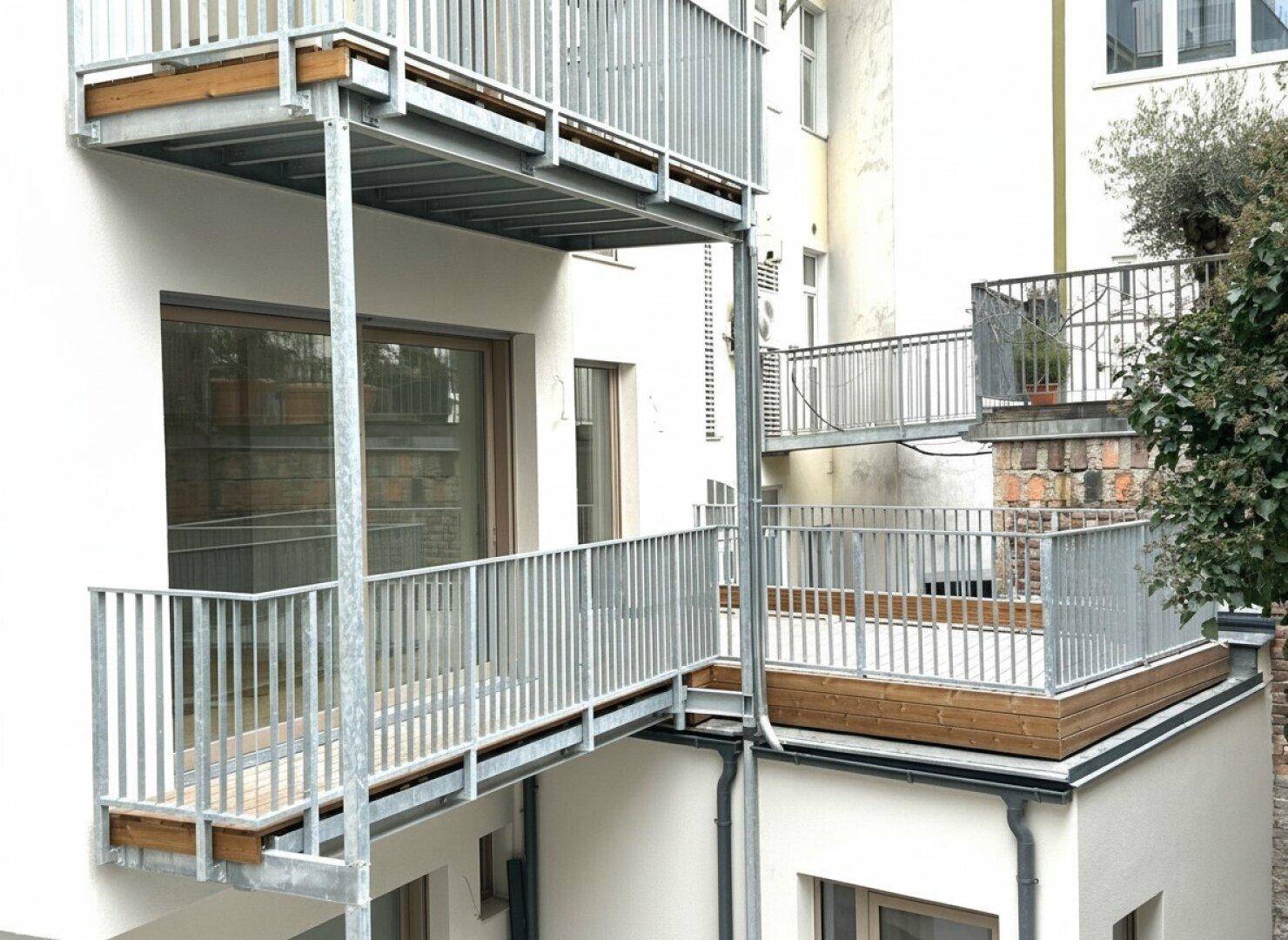 Mehrere moderne Balkone und Terrassen mit Metallgeländern an der Gebäudefassade.