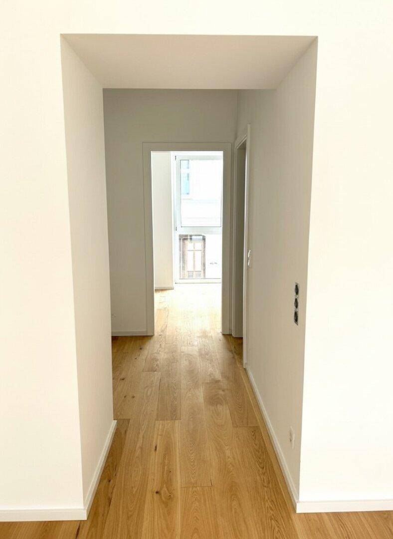 Heller Flur mit Holzboden, der zu weiteren Räumen und einem Fenster am Ende führt.