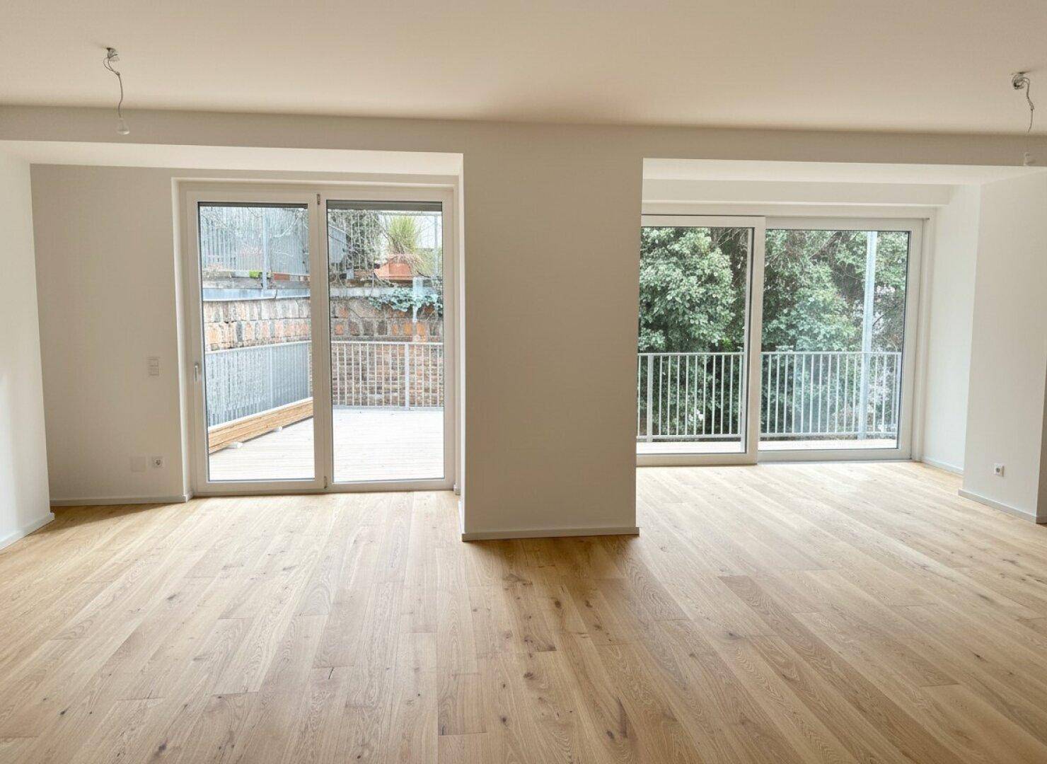 Lichtdurchflutetes Wohnzimmer mit neuem Holzboden und zwei Zugängen zu Balkonen oder Terrassen.