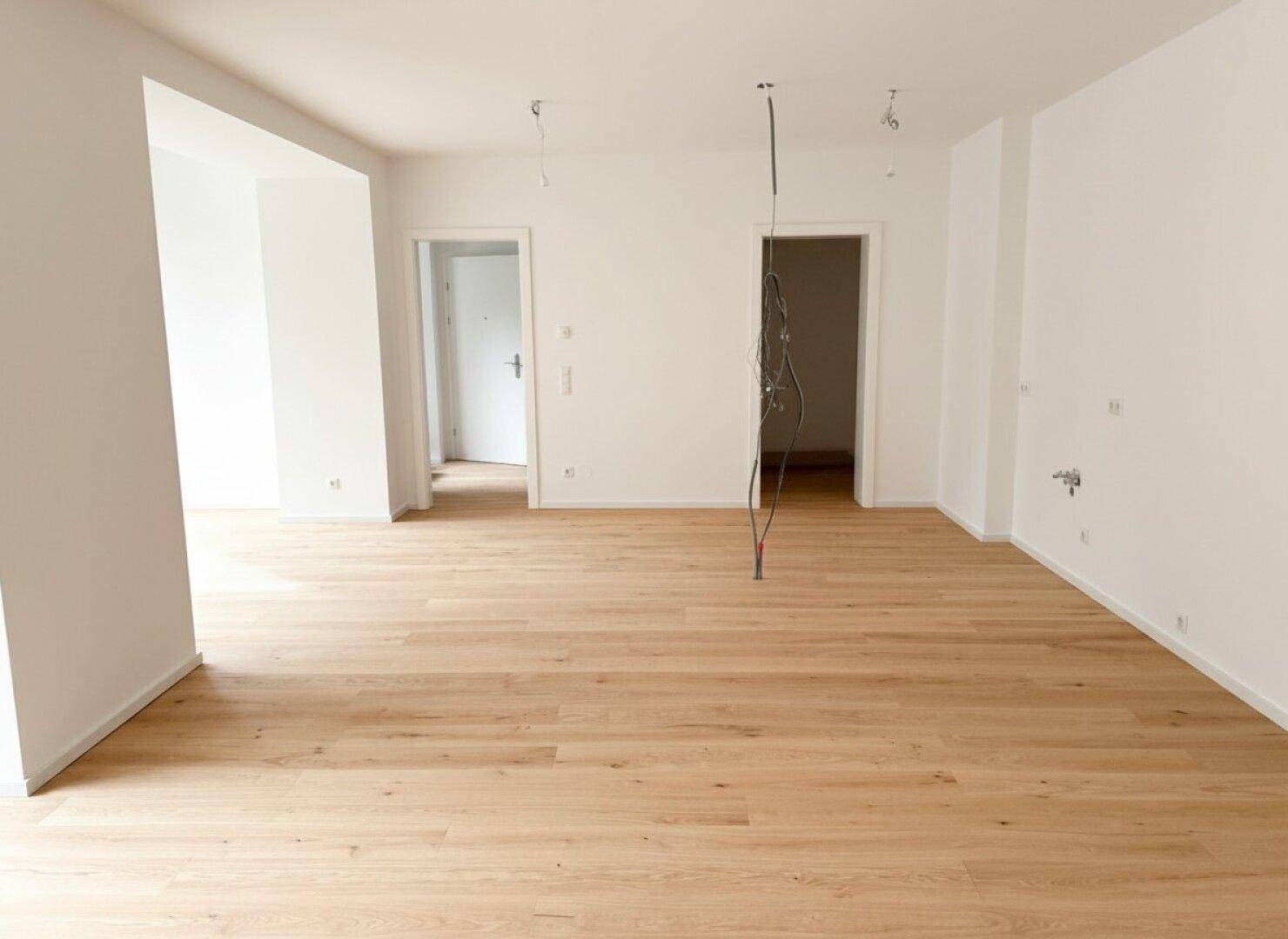 Heller, leerer Raum mit Holzboden und weißen Wänden, ideal für einen offenen Wohnbereich.