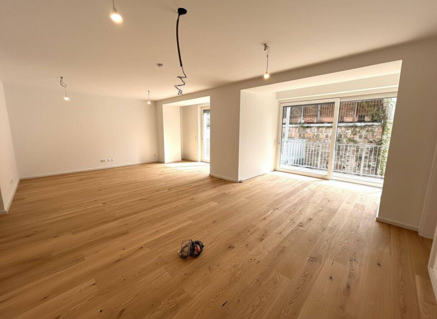 Heller Wohnbereich mit Holzboden und breiten Fensterfronten, die den Raum lichtdurchfluten.