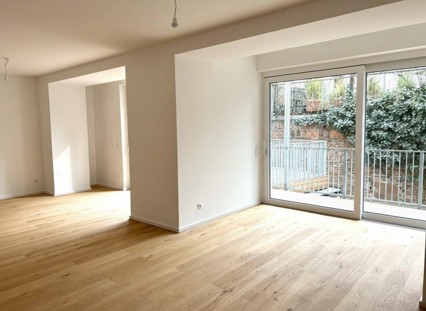 Großzügiger Wohnraum mit Eichenparkett und Zugang zu einer Terrasse, umgeben von Grün.