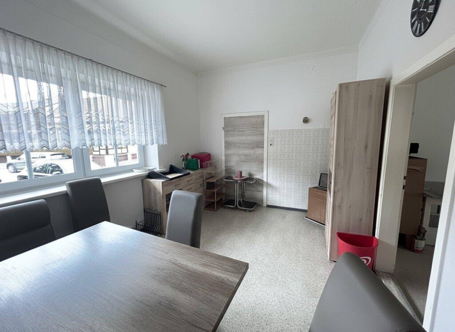 Geräumiger Essbereich mit Fenster, Möbeln und einem Durchgang zu einem weiteren Raum, gut beleuchtet.