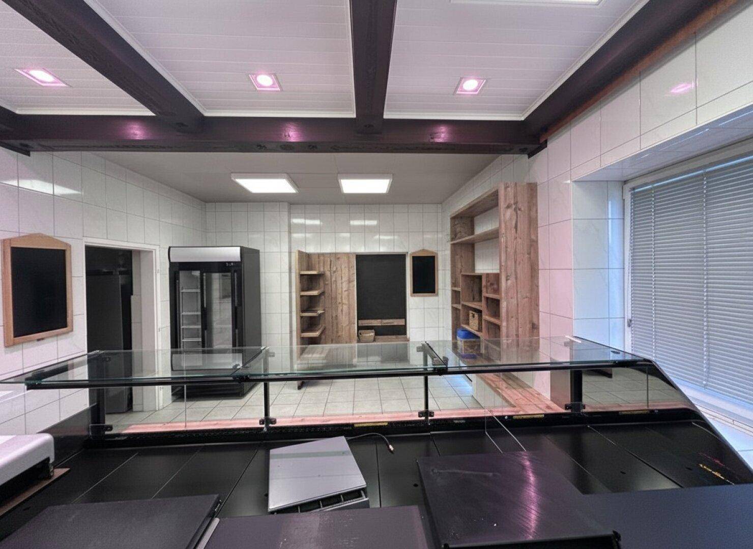 Gewerbefläche mit gefliesten Wänden, Holzbalkendecke und modernen Verkaufstheken aus Glas und Holz.