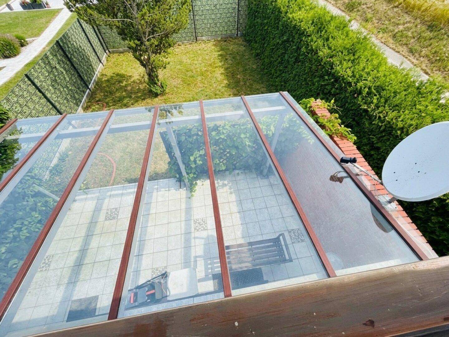 Blick von oben auf die überdachte Terrasse und den angrenzenden Gartenbereich mit Rasen.