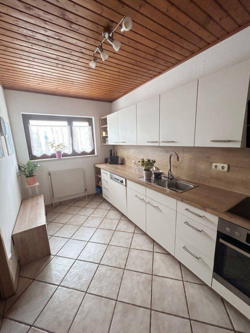 Moderne Küche mit weißen Schränken, Holzdecke und Fliesenboden, ausgestattet mit Geräten.