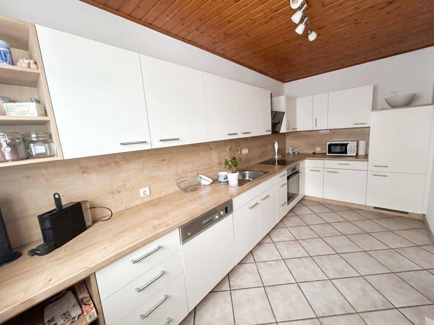 Helle Küche mit weißen Fronten, Holzdecke und Fliesenboden, bietet viel Arbeitsfläche.