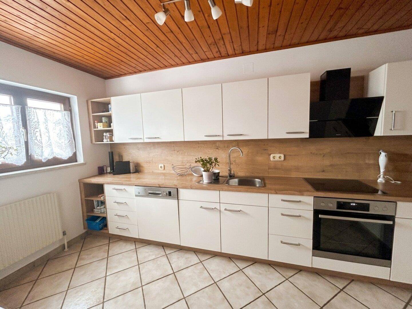 Funktionale Küche mit weißen Schränken, Holzdecke und Fliesenboden, inklusive Kochfeld und Backofen.