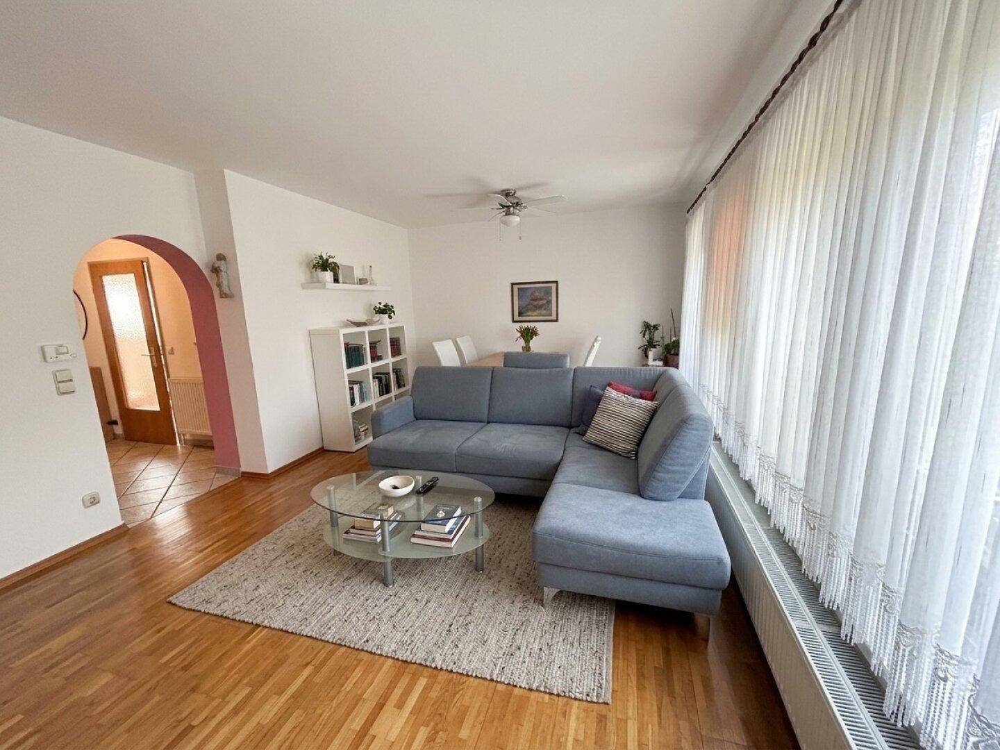 Helles Wohn-Esszimmer mit Parkettboden, einem großen Sofa und einem Esstisch im Hintergrund.