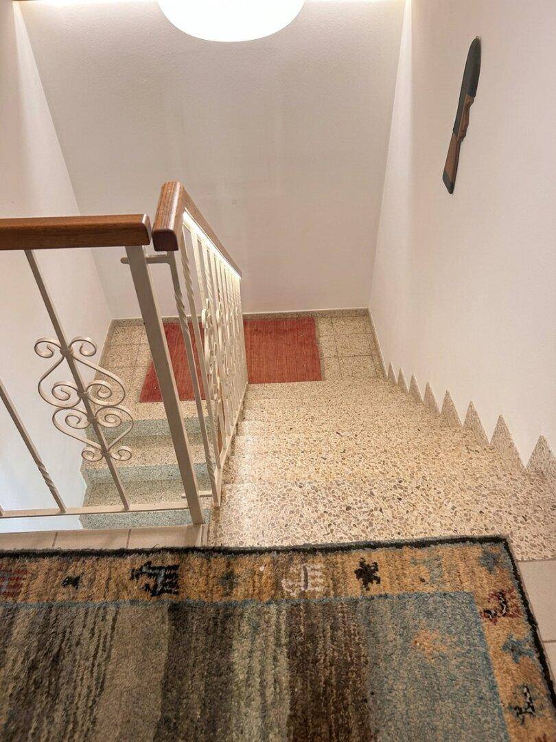 Treppenhaus mit Terrazzostufen und einem dekorativen Geländer, das in die obere Etage führt.