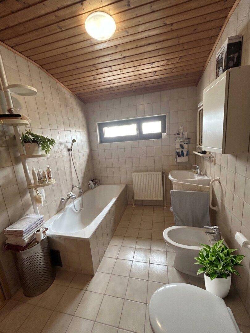 Helles Badezimmer mit Badewanne, WC, Bidet und einem Fenster für natürliche Belüftung.