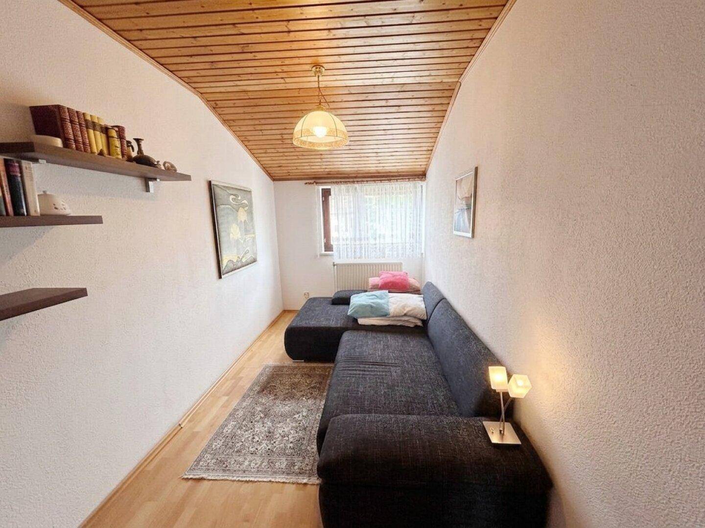 Kleines Schlafzimmer mit Holzbalkendecke, Sofa und einem Fenster für natürliches Licht.