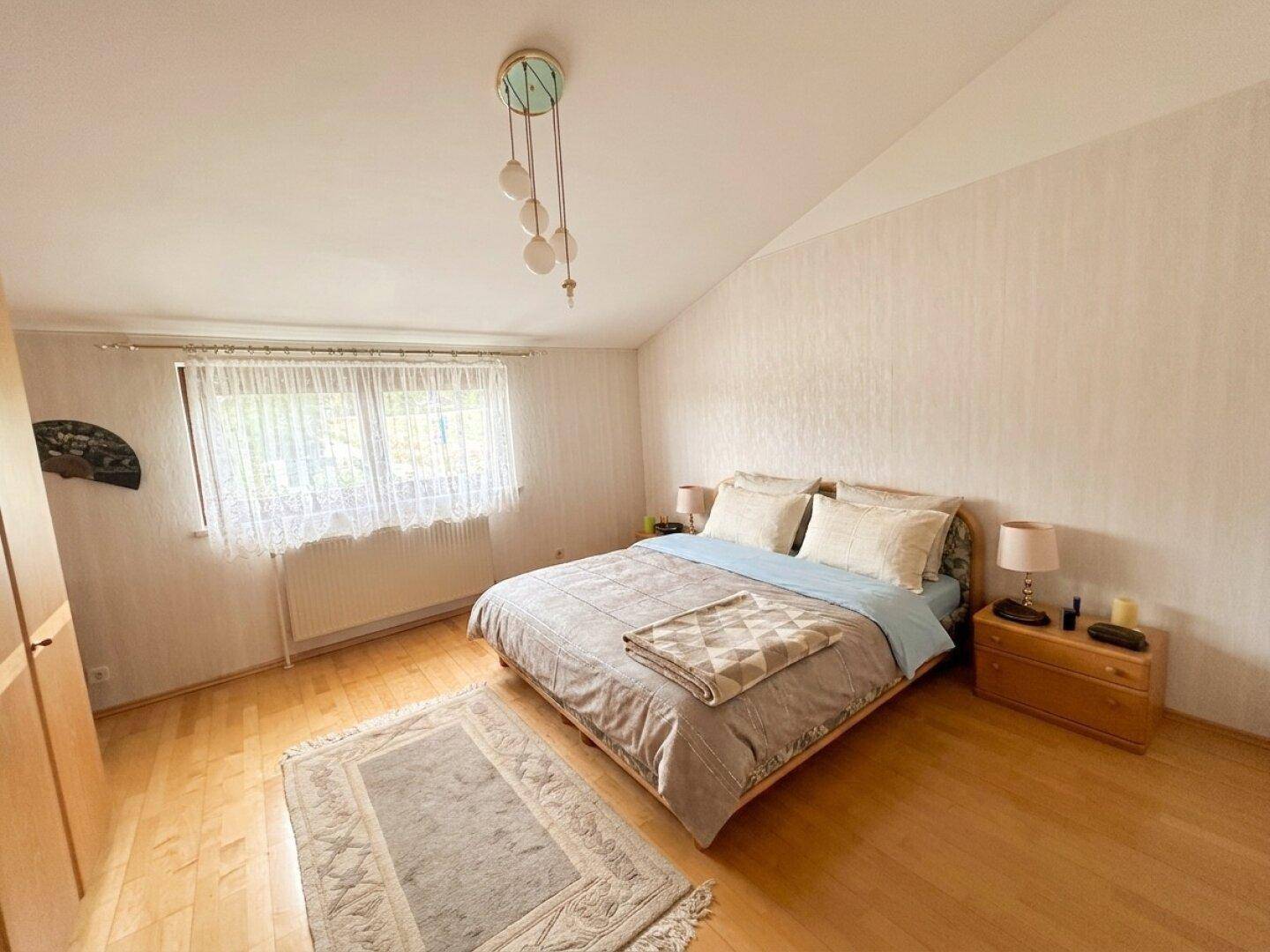 Gemütliches Schlafzimmer mit Doppelbett, Parkettboden und einem Fenster mit Vorhängen.