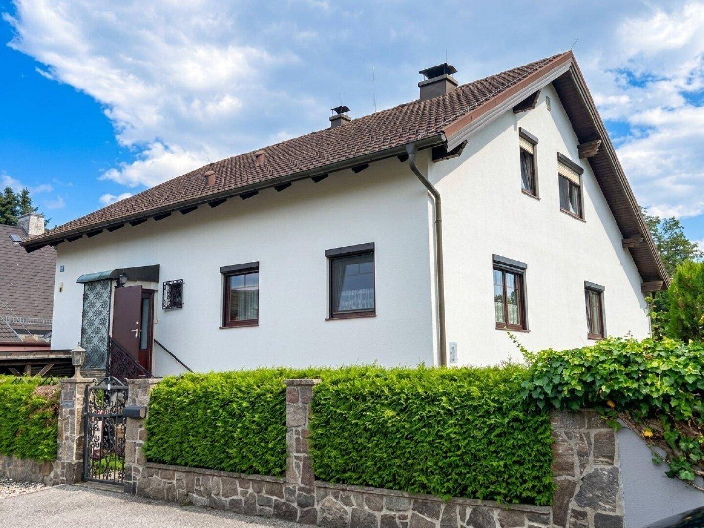 Ansicht des Hauses von der Straße mit gepflegter Hecke und Steinmauer im Vorgartenbereich.