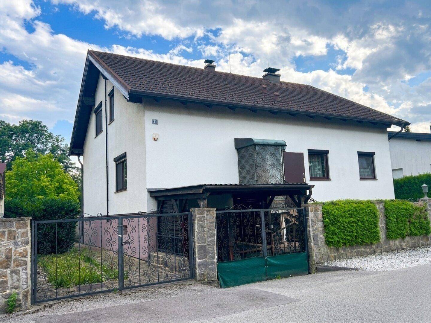 Seitenansicht des Hauses mit überdachtem Eingangsbereich und schmiedeeisernem Tor zur Grundstückszufahrt.