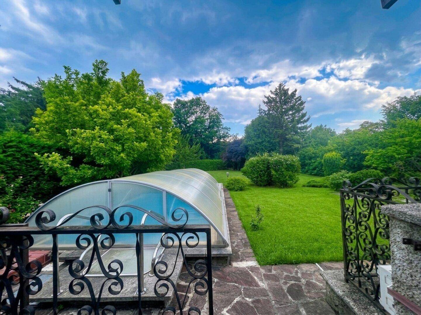 Blick auf den überdachten Pool und den weitläufigen Gartenbereich mit üppiger Vegetation.