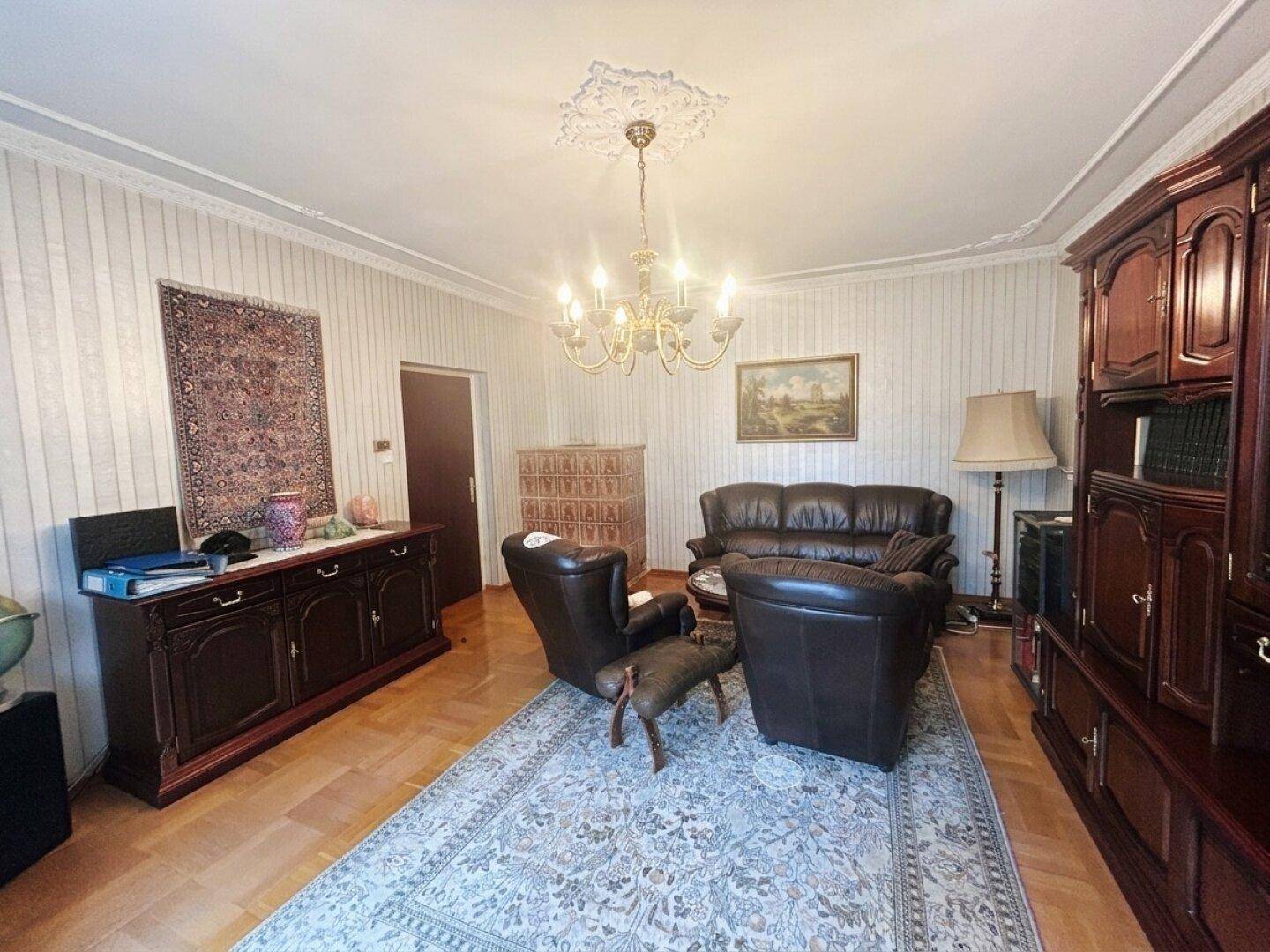 Klassisch eingerichtetes Wohnzimmer mit dunklen Holzmöbeln, Ledersofas und einem großen Teppich.