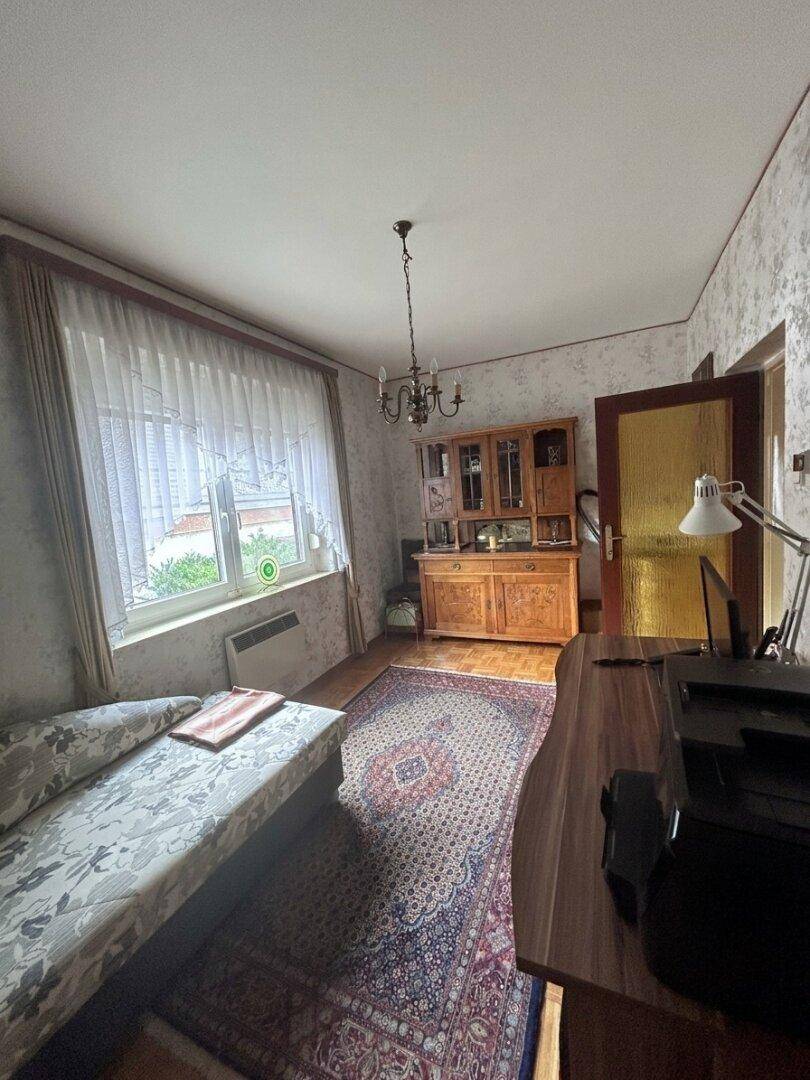 Helles Arbeitszimmer mit Schreibtisch, Bett und Holzschrank, ideal als Gäste- oder Bürozimmer.