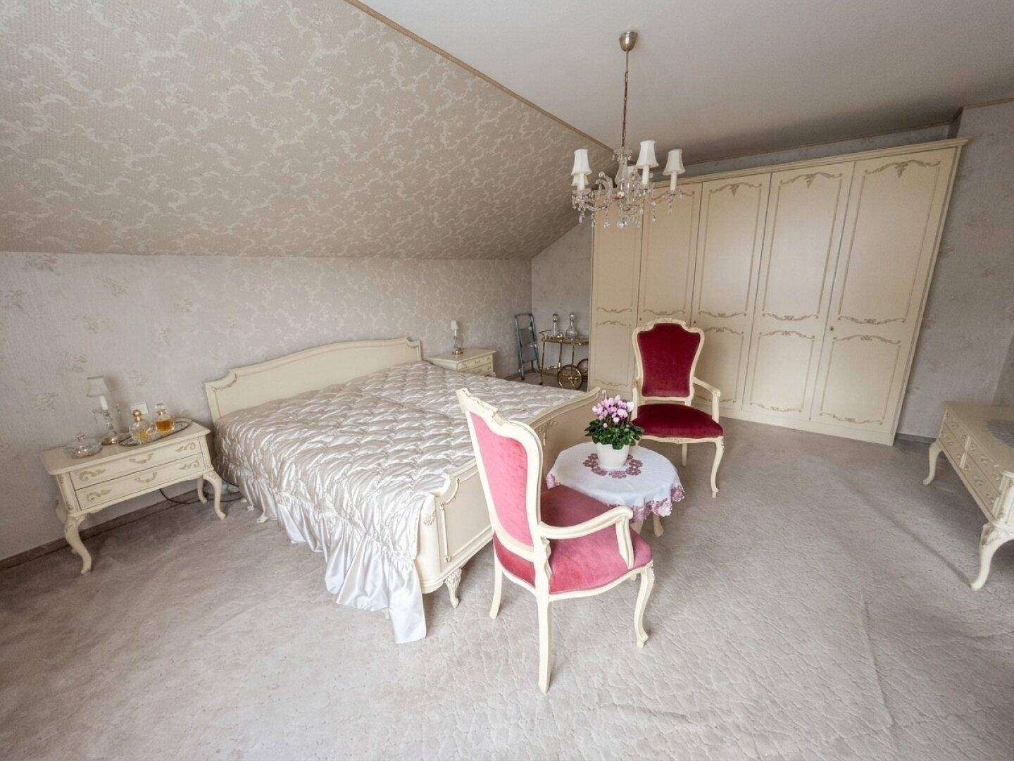 Geräumiges Schlafzimmer mit großem Bett, eleganten Stühlen und Einbauschränken unter der Dachschräge.