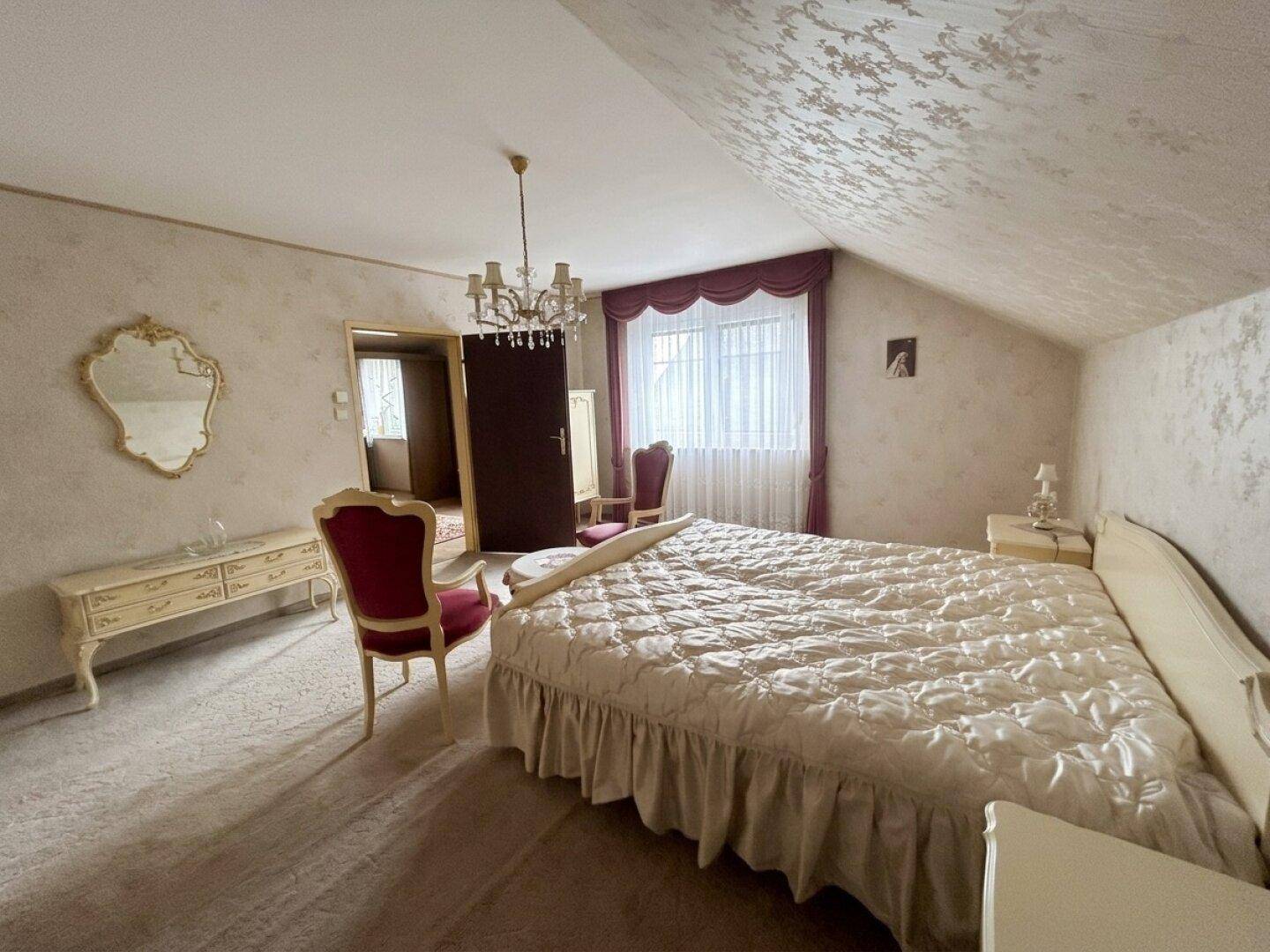 Helles Schlafzimmer mit großem Bett, Spiegel und Fenster, das viel Tageslicht hereinlässt.