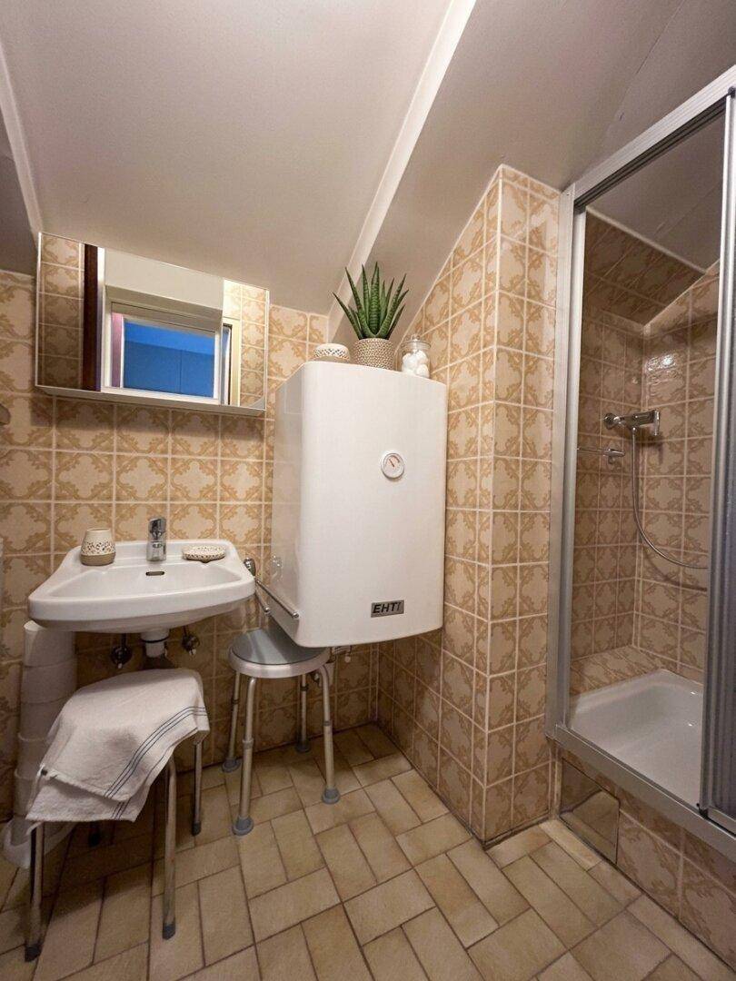 Badezimmer mit beigefarbenen Fliesen, Duschkabine und einem wandmontierten Waschbecken.