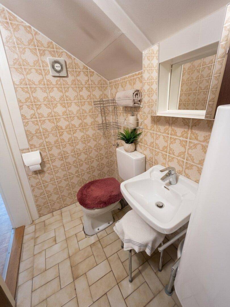 Kleines WC mit beigefarbenen Fliesen, Toilette und Waschbecken unter einer Dachschräge.