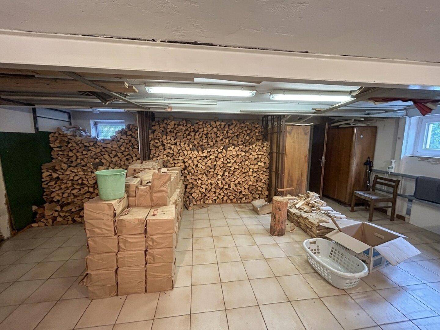 Kellerraum mit gestapeltem Brennholz und Fliesenboden, ideal als Lagerfläche.