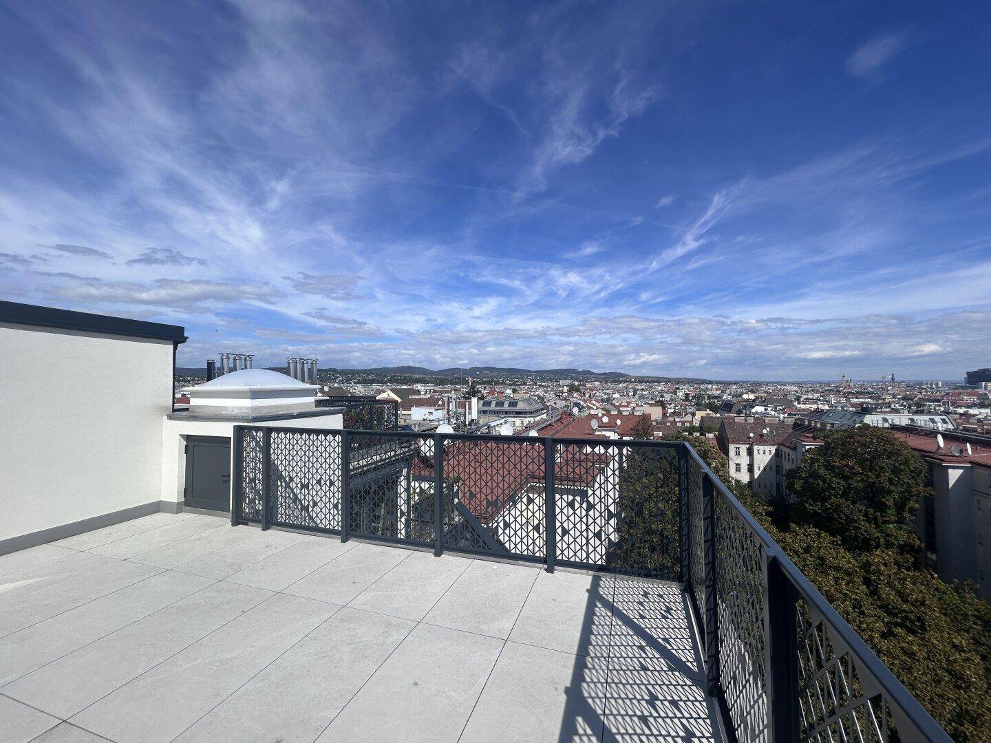 Sonnige Dachterrasse mit weitem Stadtblick und sichtbaren Hügeln am Horizont unter klarem Himmel.