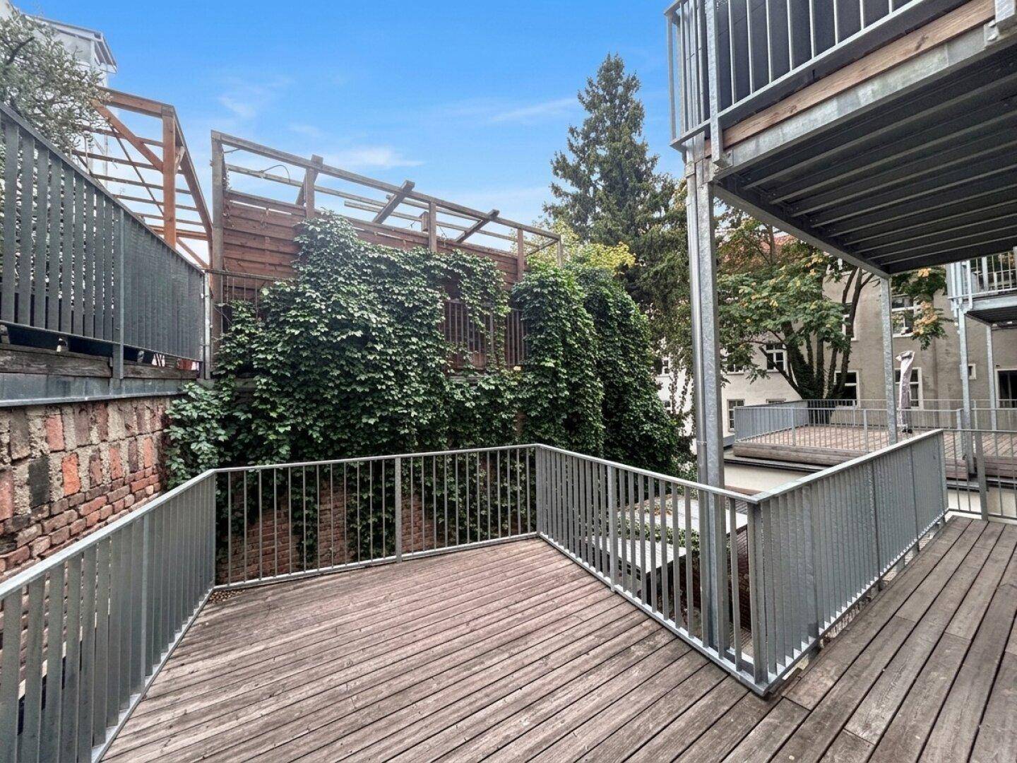 Geräumige Holzterrasse mit Metallgeländer und einer grünen, mit Efeu bewachsenen Wand im Hintergrund.