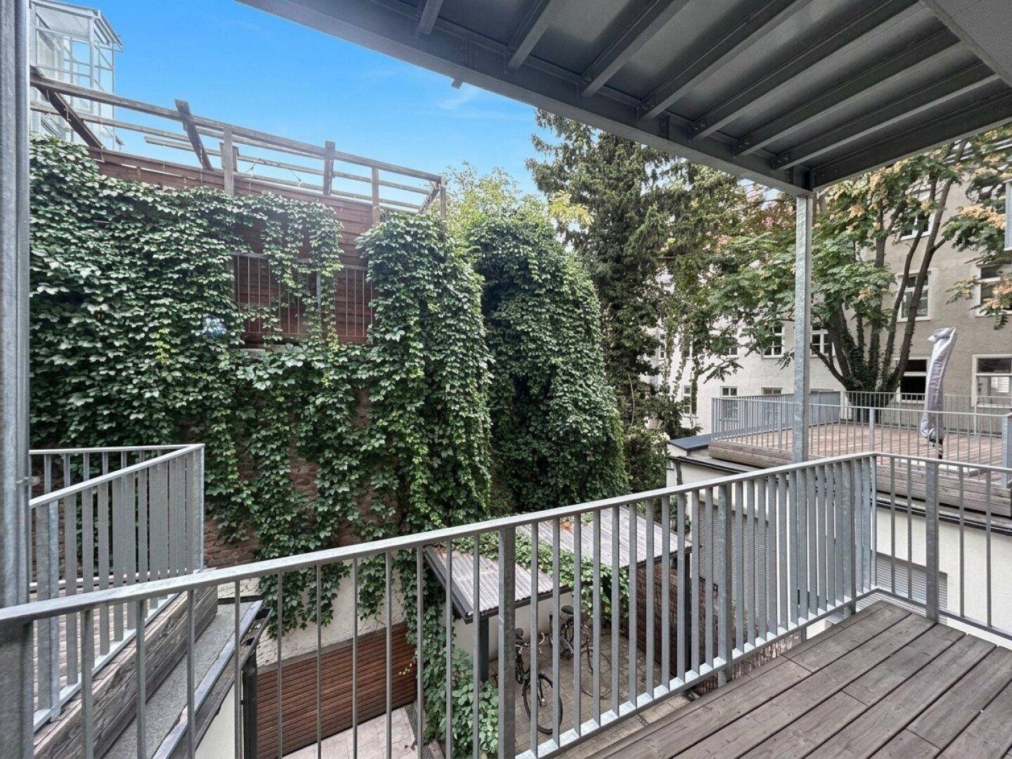 Blick von einem Balkon auf einen begrünten Innenhof mit Fahrradunterstand und Efeu an den Wänden.