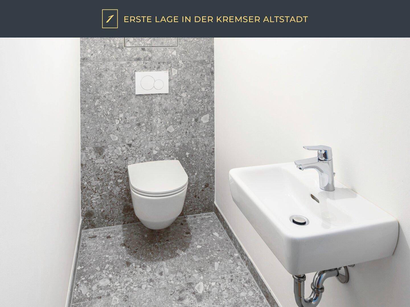 Gäste-WC mit modernen grauen Fliesen, wandhängendem WC und kleinem Waschbecken.