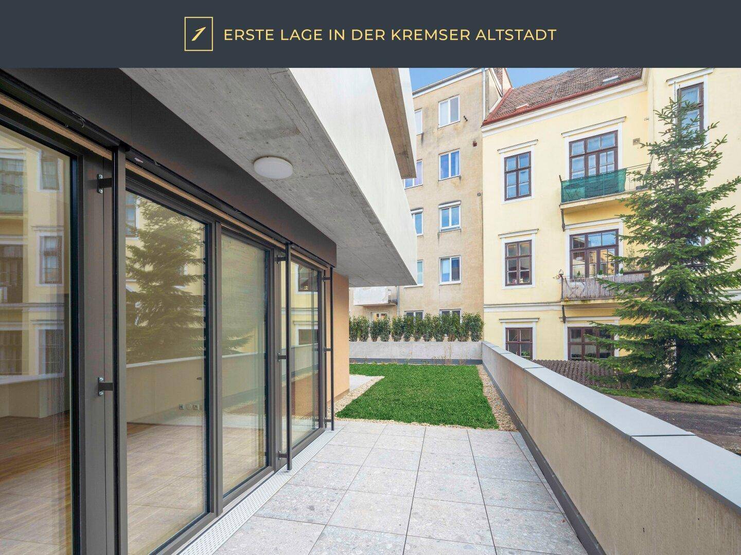 Terrasse mit Fliesenboden und angrenzender Rasenfläche, umgeben von Gebäuden.