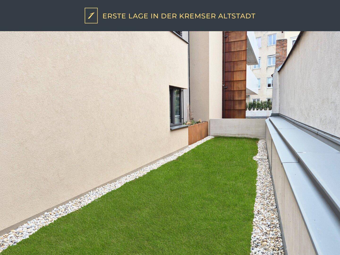 Schmaler Gartenstreifen mit Rasen und Kiesweg entlang der Gebäudewand.