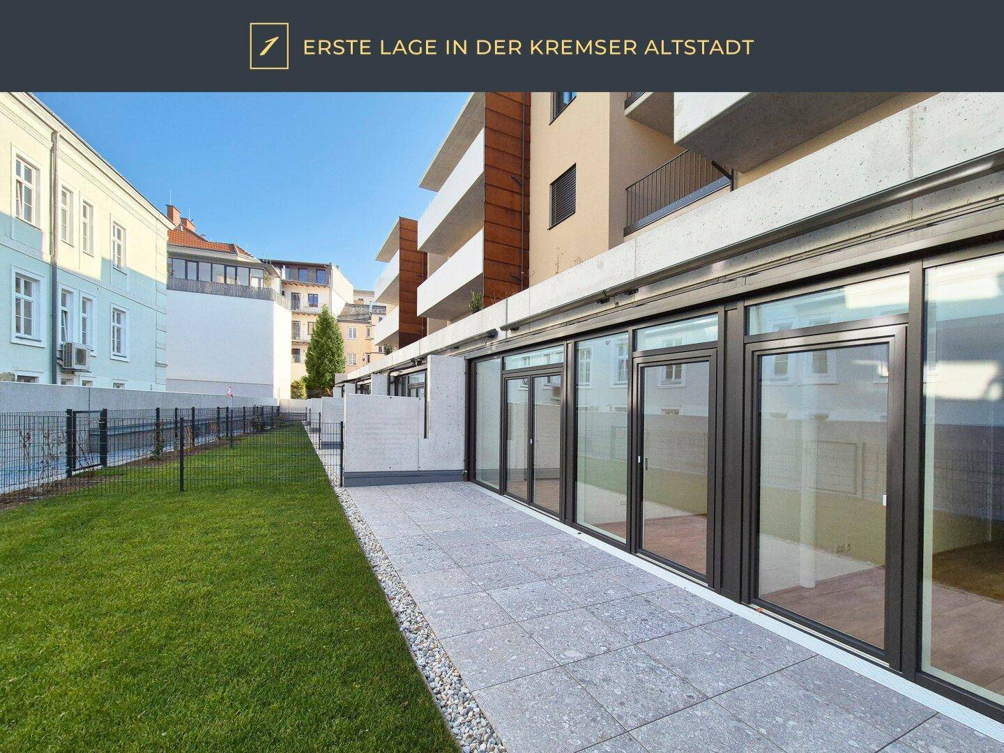 Moderne Terrasse mit Fliesenboden und angrenzender Rasenfläche vor dem Gebäude.