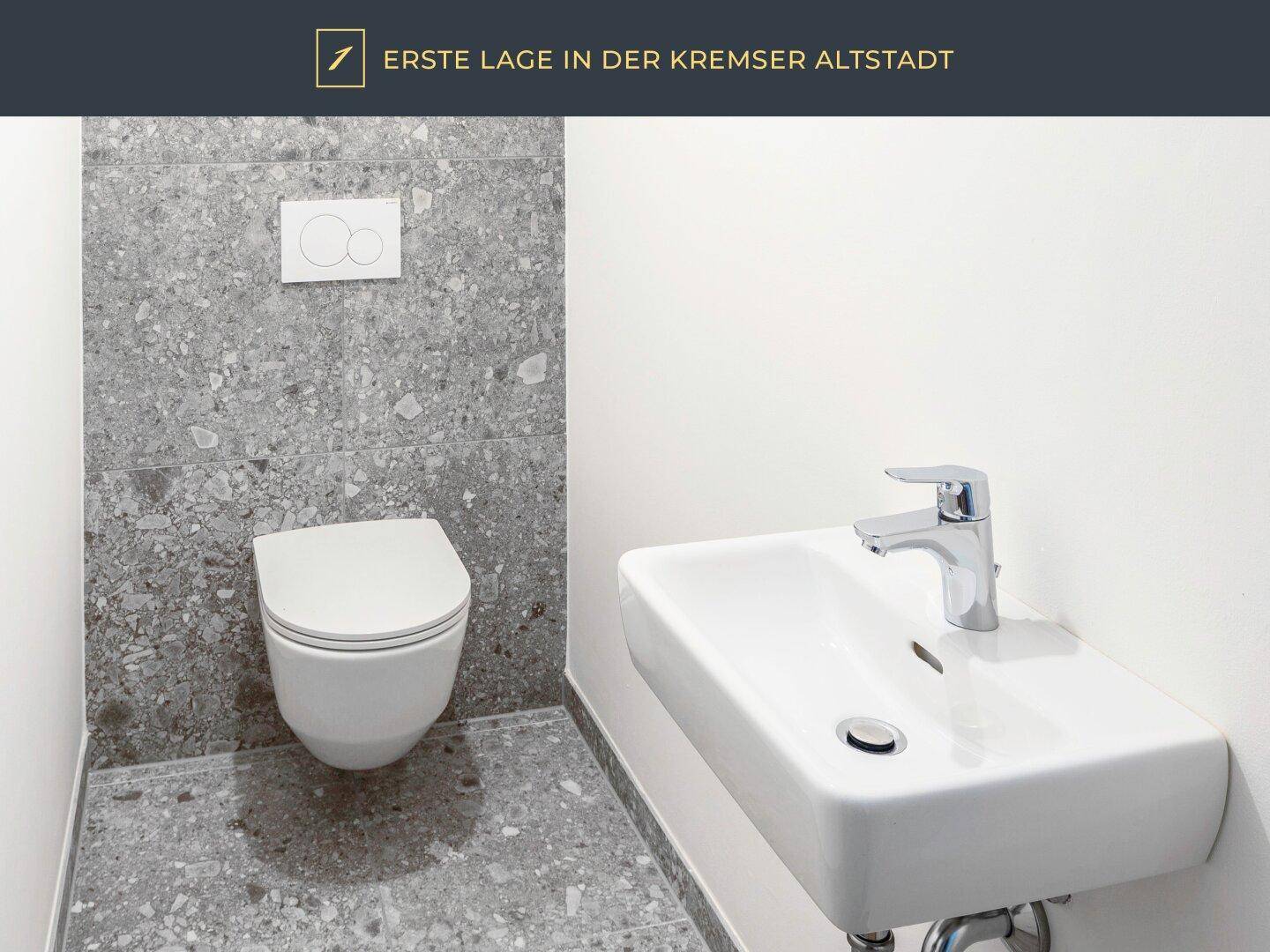 Modernes Gäste-WC mit Wand-WC und kleinem Waschbecken, graue Fliesen.