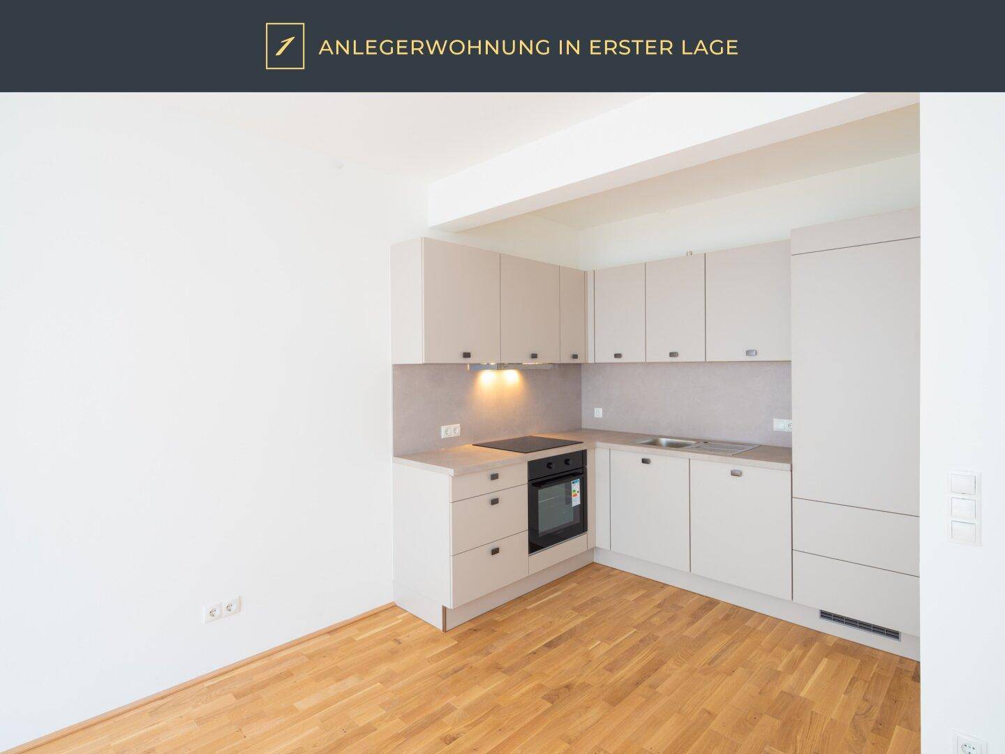 Moderne, unmöblierte Küche mit hellen Schränken, Einbaugeräten und Holzparkettboden.