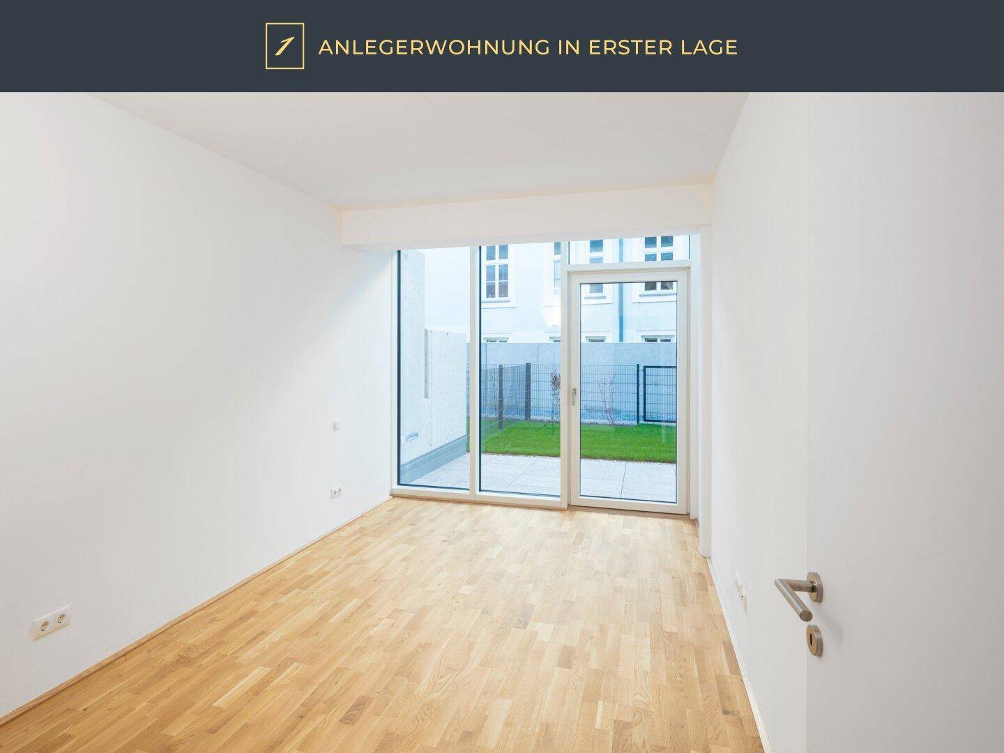 Heller, unmöblierter Raum mit Holzparkett und Zugang zu einer kleinen Grünfläche im Freien.