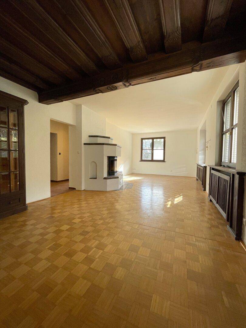 Geräumiges Wohnzimmer mit Parkettboden, Kamin und sichtbaren Holzdeckenbalken.