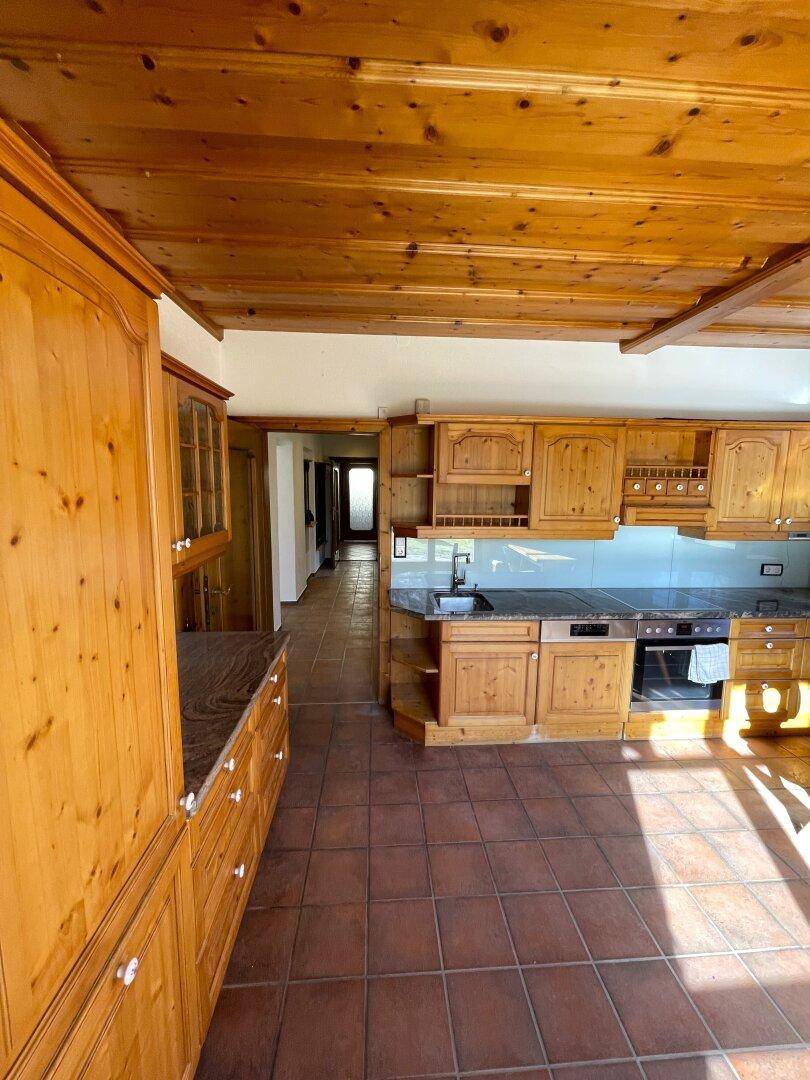Geräumige Küche mit Holzmöbeln, Terrakottafliesen und Blick in den Flur.