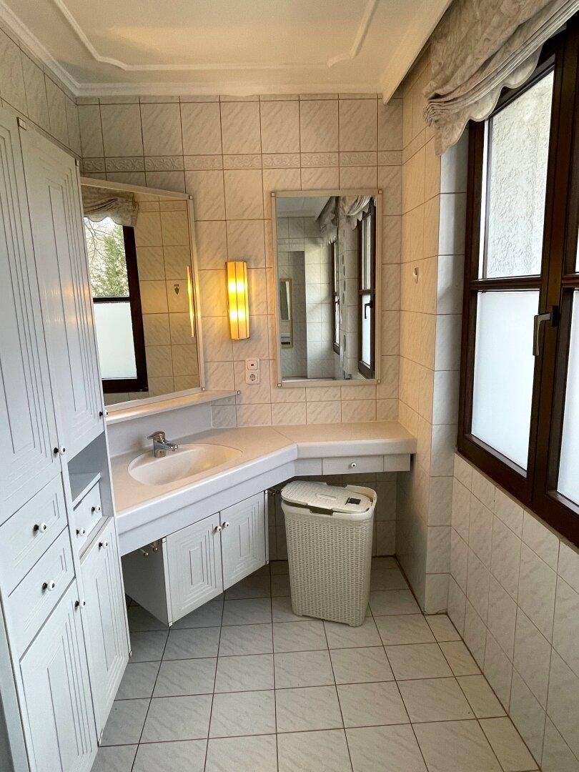 Badezimmer mit Waschtisch, Spiegelschrank und Fenster.