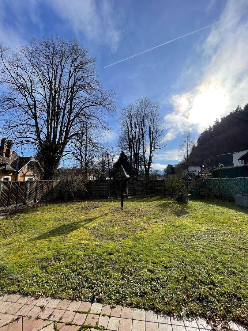 Großer Garten mit Rasenfläche und altem Baumbestand unter blauem Himmel.