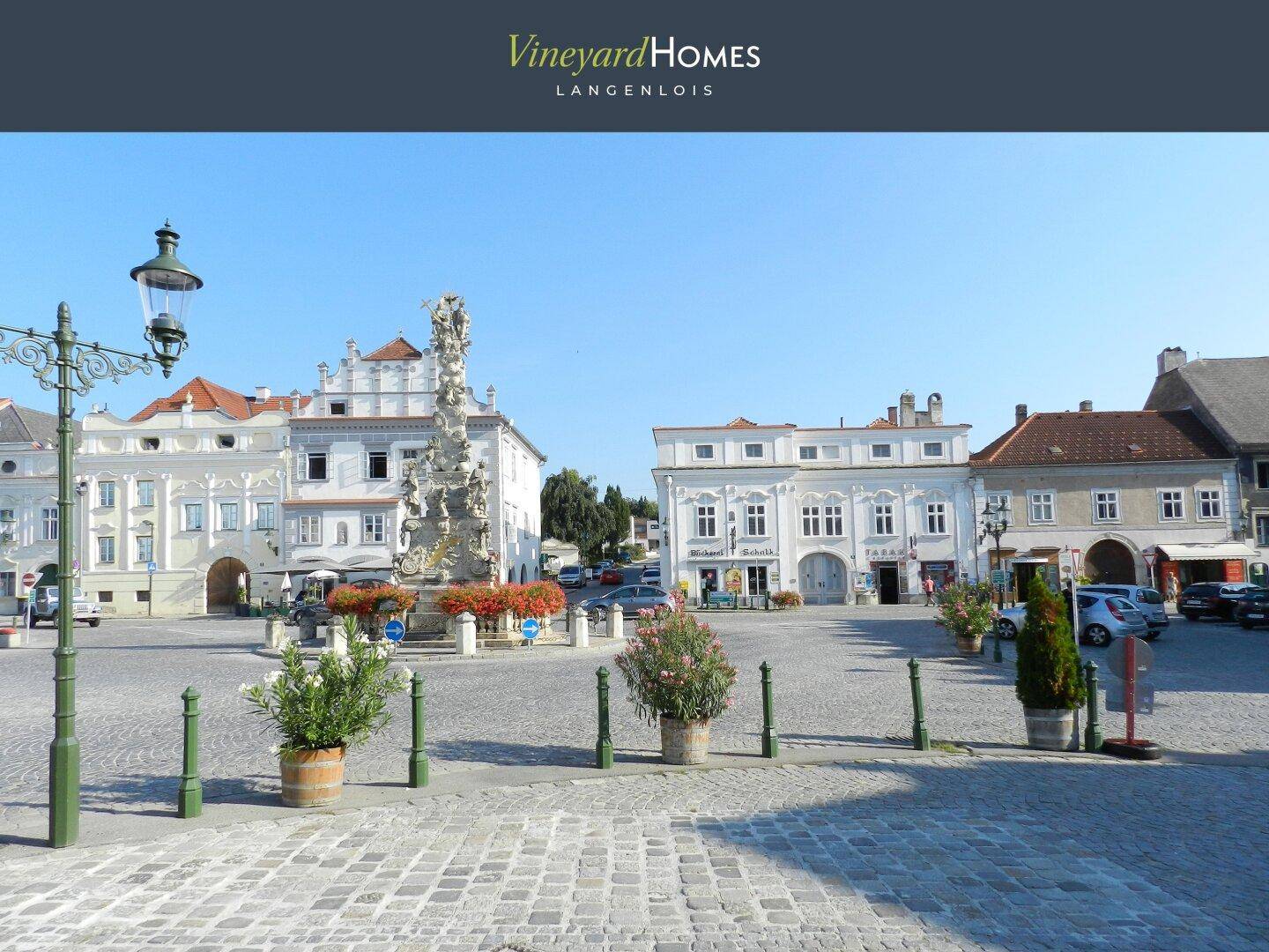 Historischer Stadtplatz mit barockem Denkmal und traditionellen Gebäuden unter blauem Himmel.