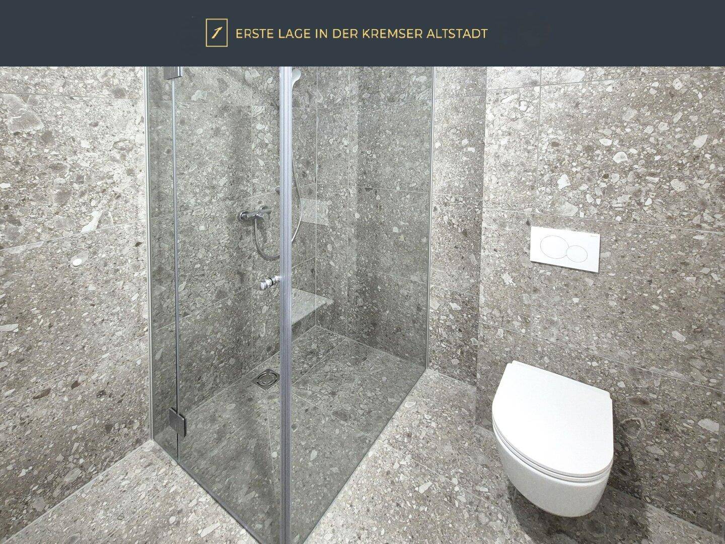 Modernes Badezimmer mit großformatigen grauen Fliesen, bodengleicher Dusche und Wand-WC.