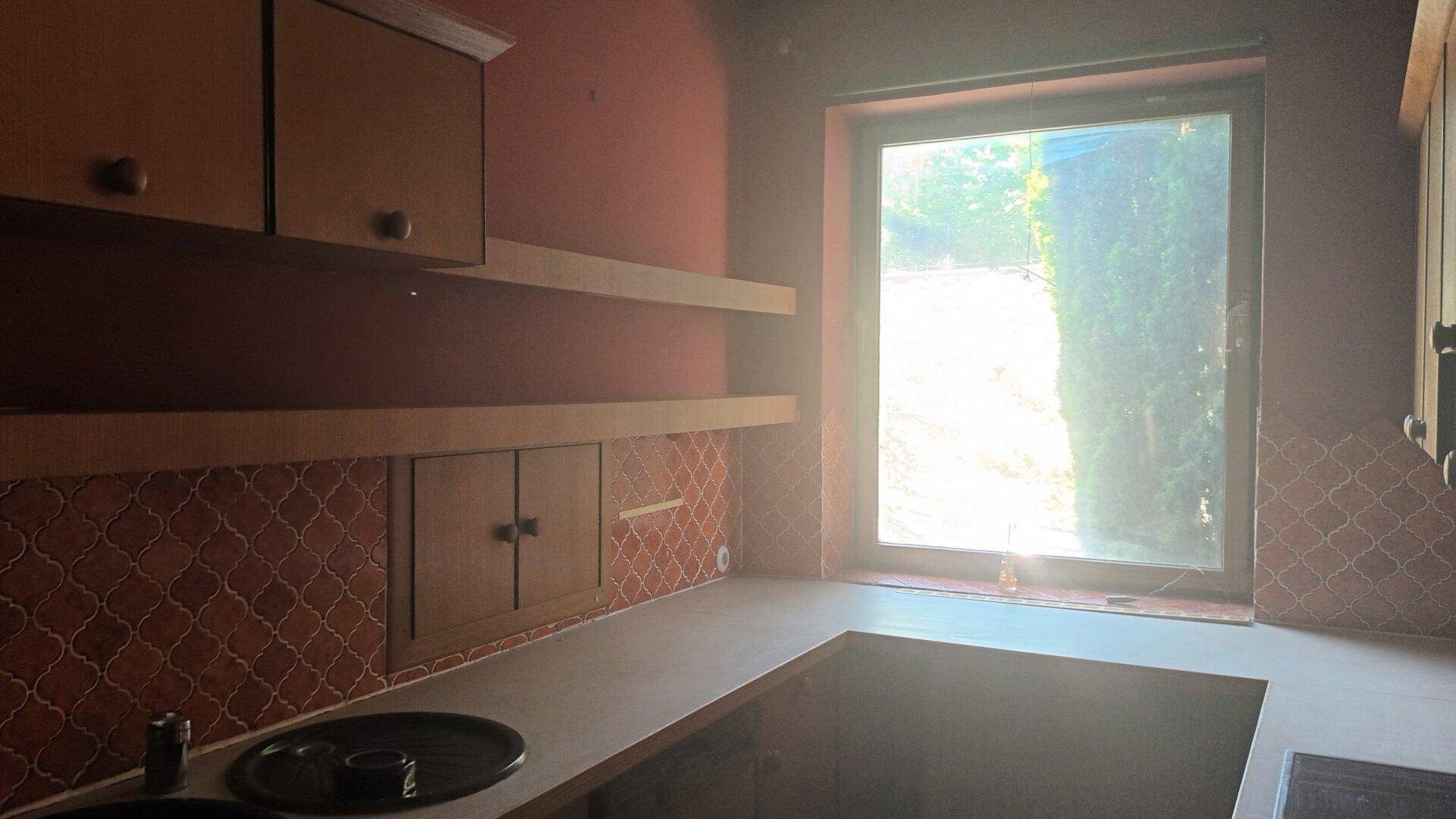 Leere Küche mit roten Wänden, Holzschränken und einem großen Fenster mit Blick ins Grüne.